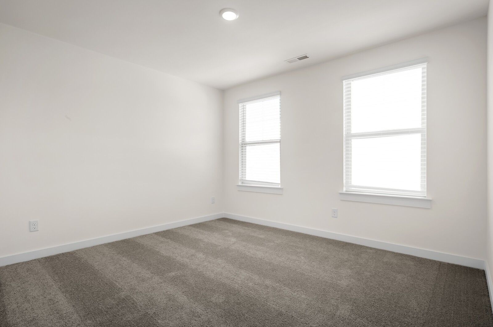 Bright, carpeted bedroom with neutral walls and two large windows in The Ash A floor plan at Woods Crossing, Gallatin.