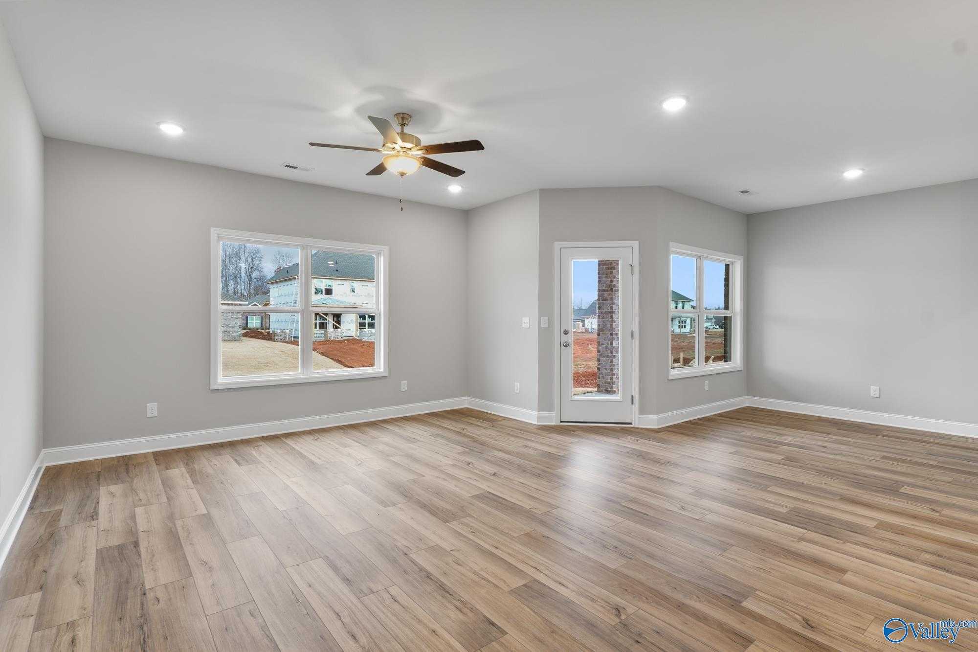 Bright living room with gray walls, hardwood floors, ceiling fan, large windows, and glass door in Davidson Homes The Daphne D, Athens AL