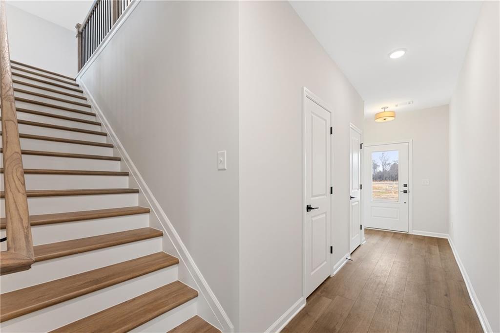 Elegant oak staircase with white railing in light gray hallway, hardwood floors, front entry door in The Rabun C 4-bedroom home, Winder, GA