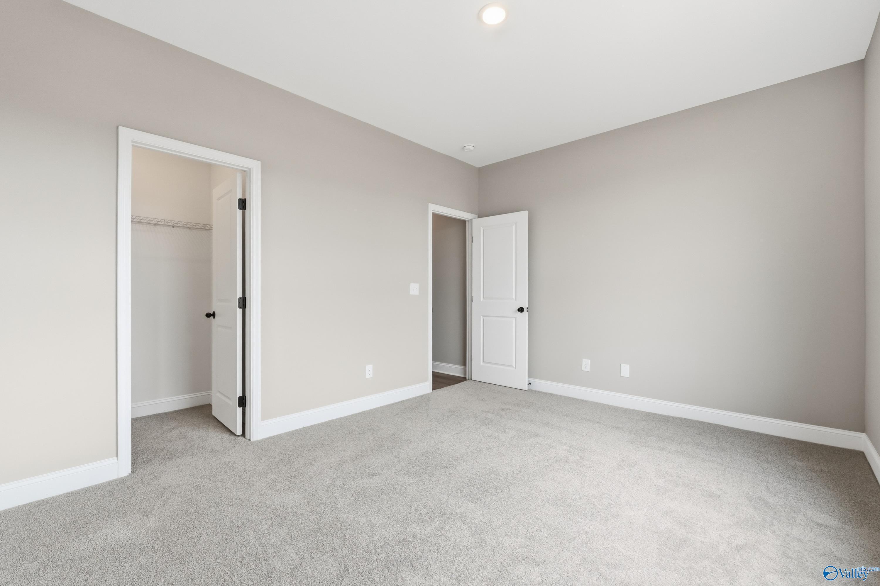 Spacious empty bedroom with light gray walls, white doors, and plush carpet in Davidson Homes The Rockford C, Athens, Alabama