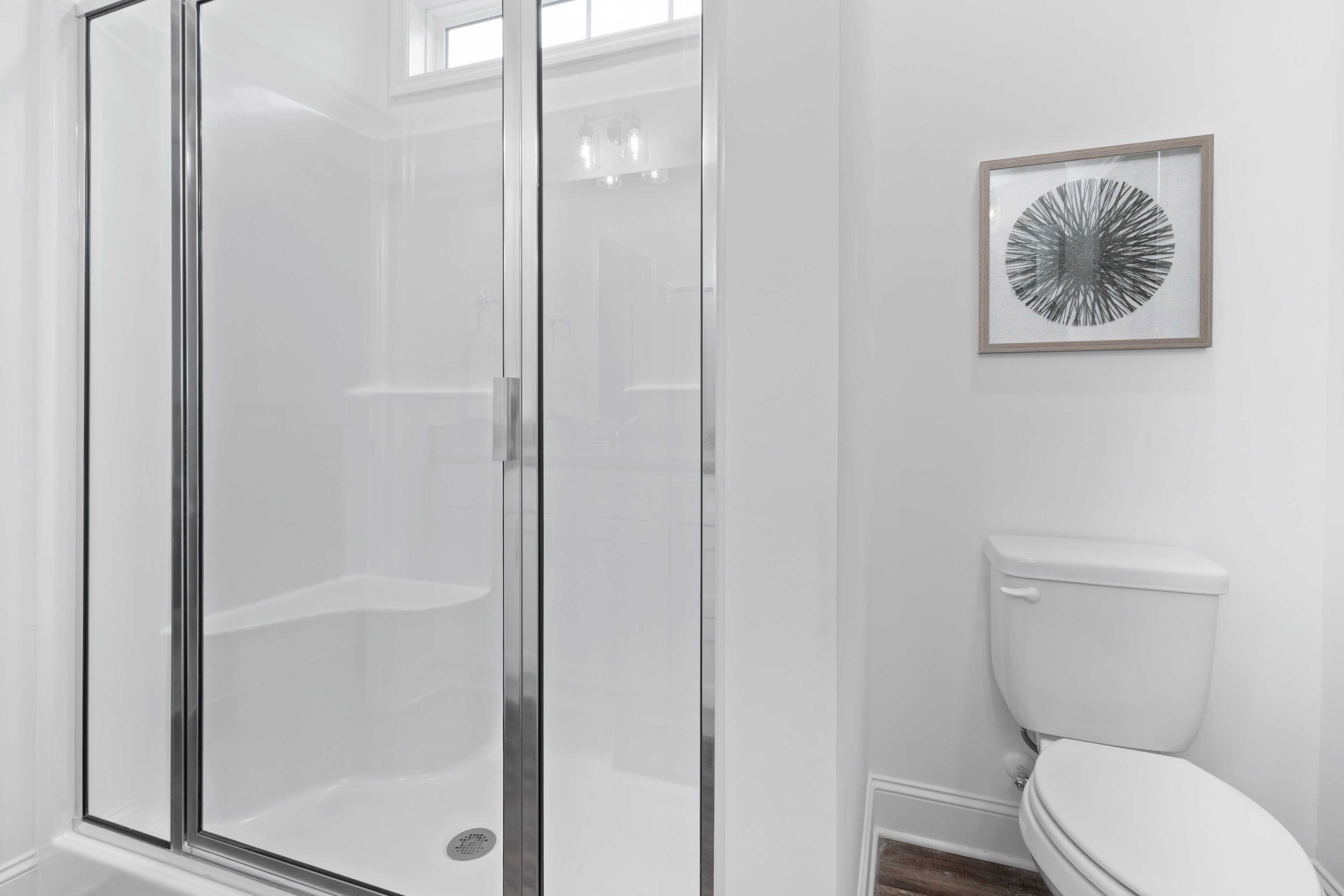 Spacious white bathroom at The Retreat at Hollon Meadow in Decatur AL with glass shower enclosure, toilet, and framed wall art