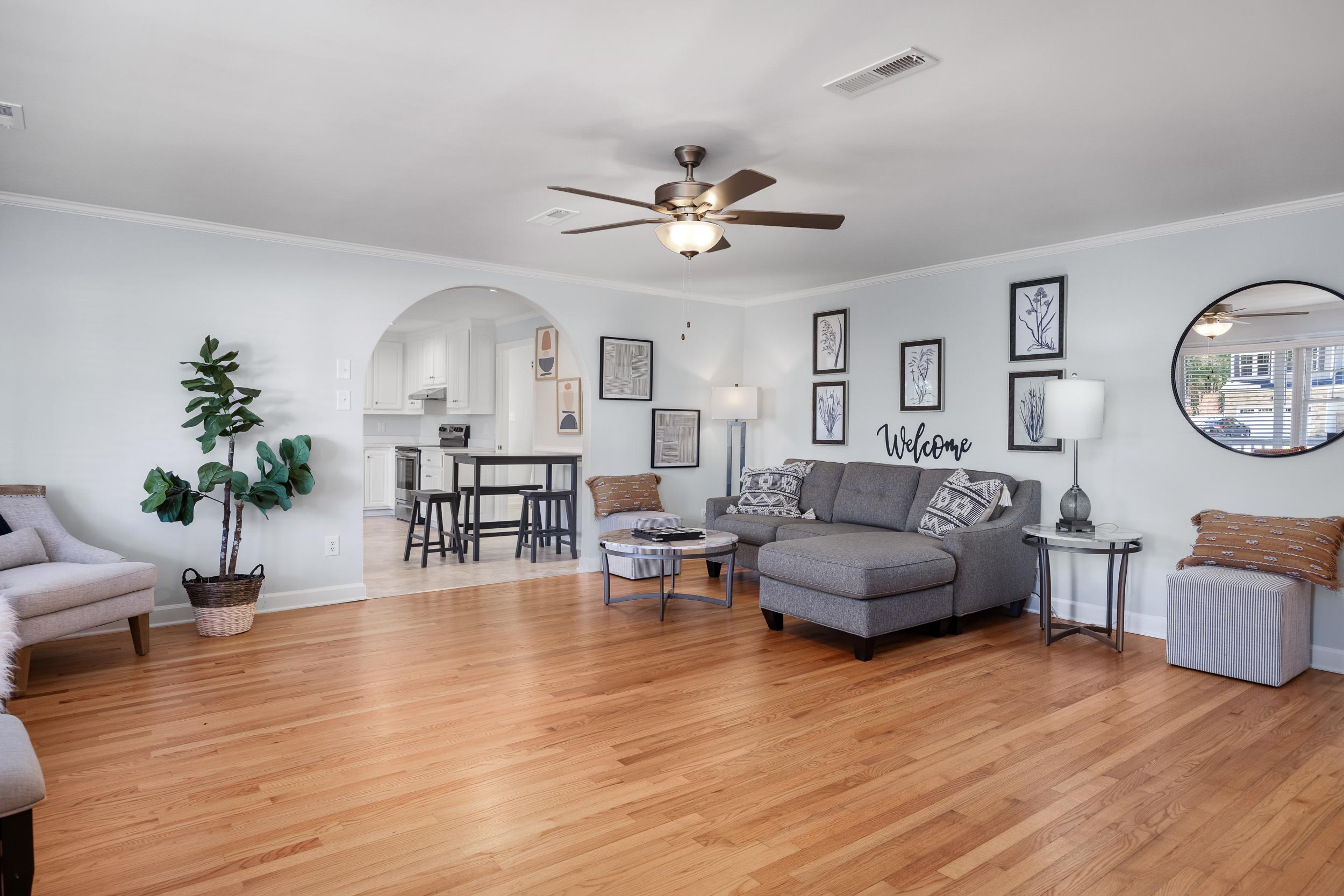 Spacious open-concept living room in Stagecoach Corner, Mebane NC with hardwood floors, gray sectional sofa, potted plant, and kitchen archway