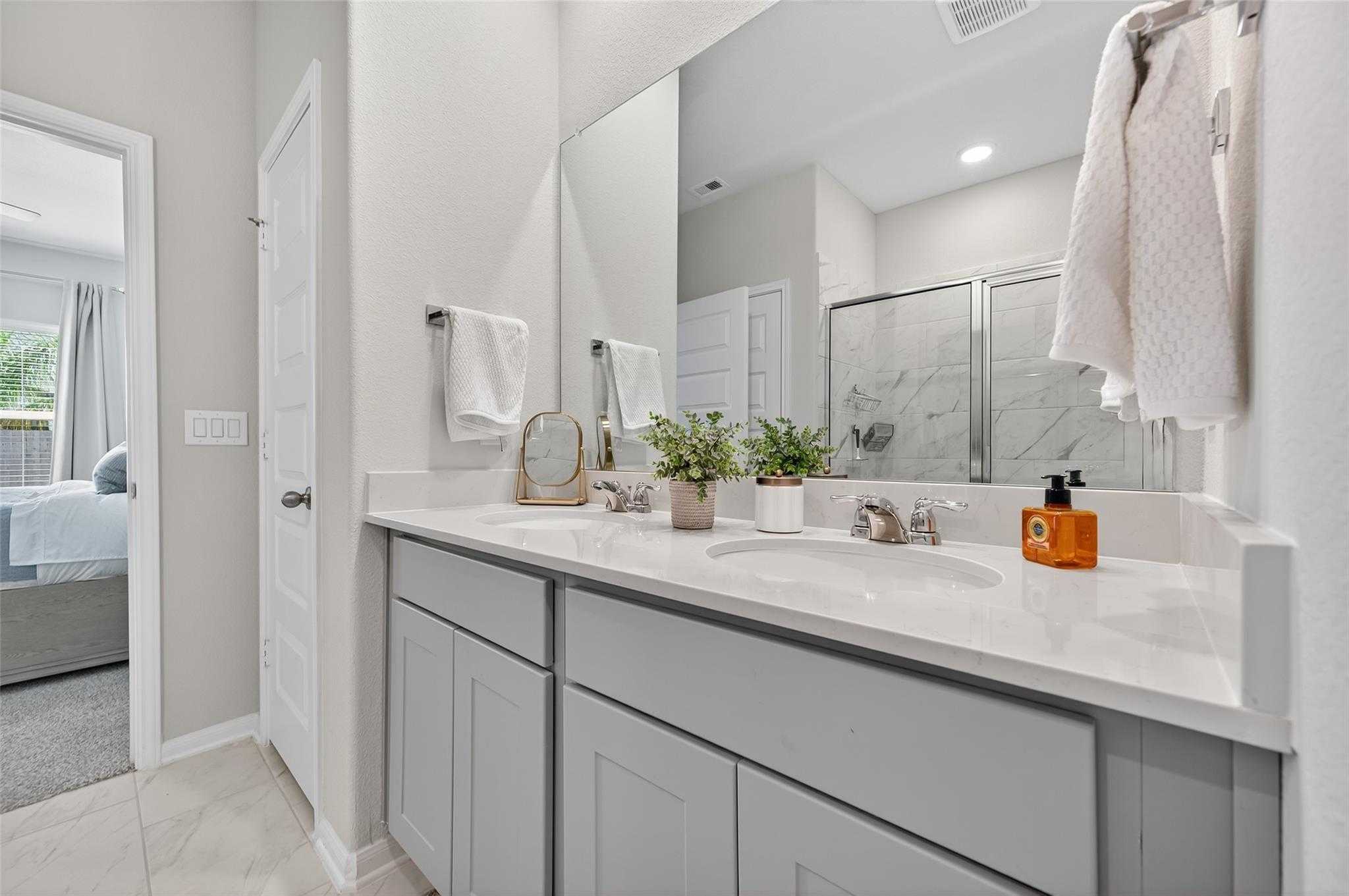 Modern master bathroom featuring double vanity with quartz counters, gray shaker cabinets, and glass shower in Davidson Homes The Brazos E, Magnolia, Texas