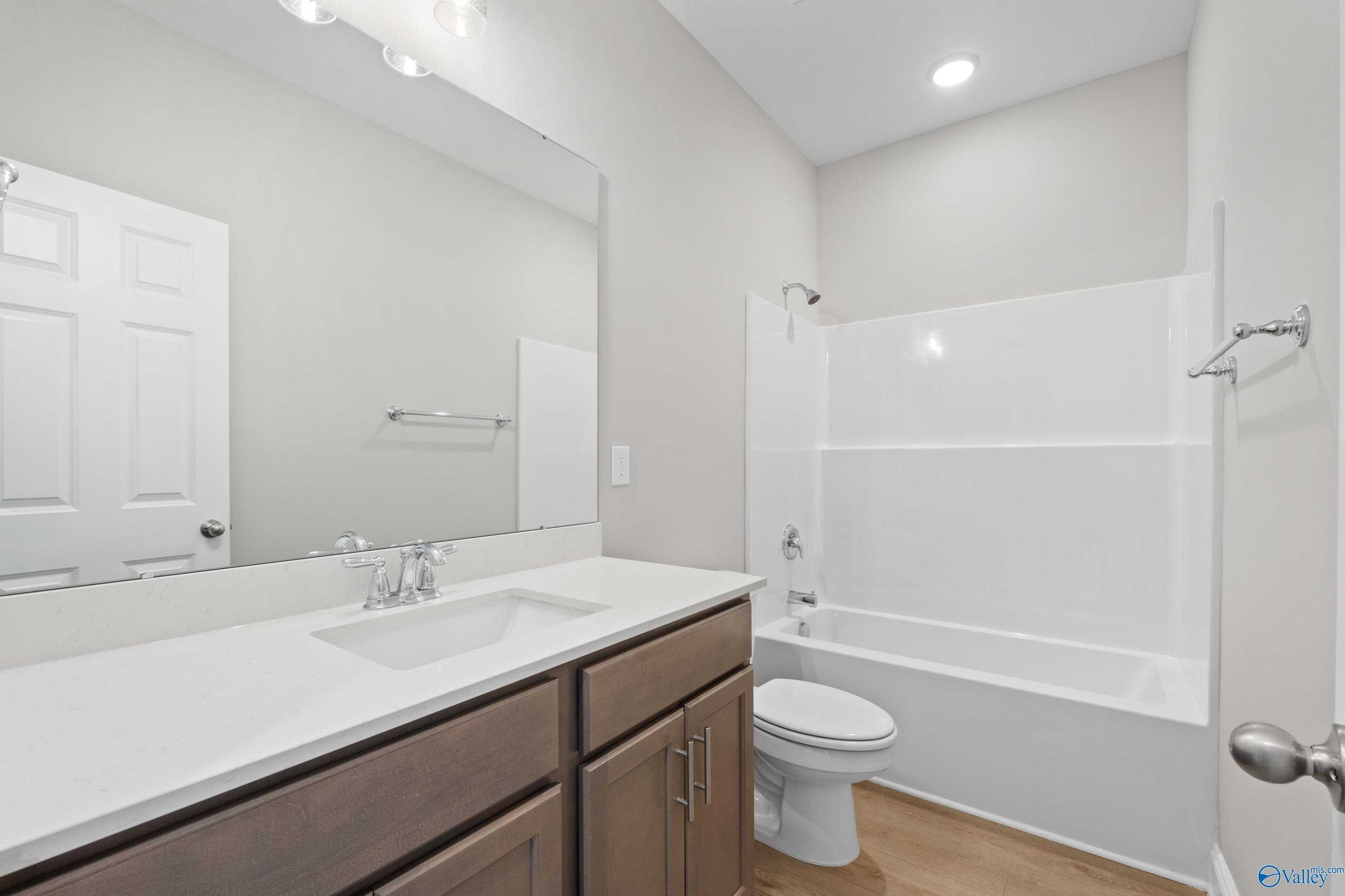 Spacious secondary bathroom with tub-shower combo, white vanity, and wood floors in Davidson Homes The Asheville C, Athens, Alabama
