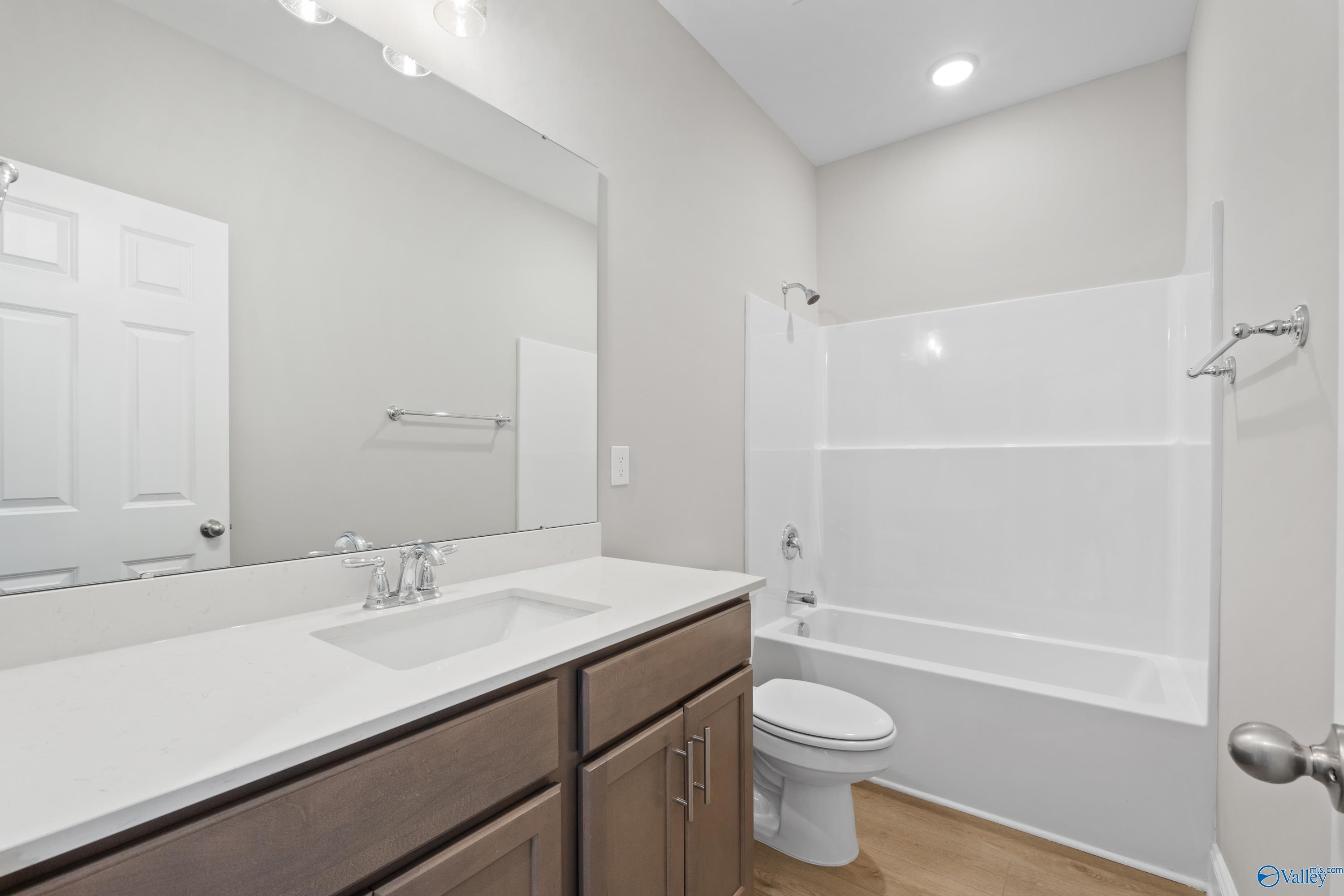 Spacious secondary bathroom with tub-shower combo, white vanity, and wood floors in Davidson Homes The Asheville C, Athens, Alabama