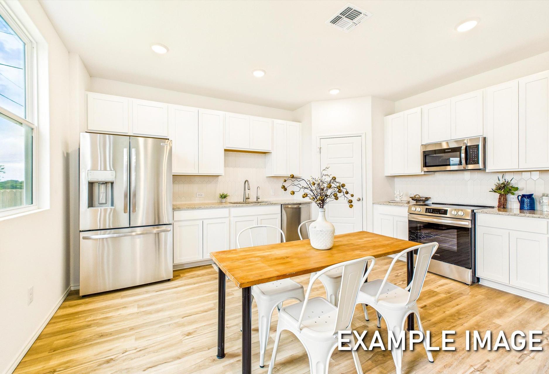 Modern kitchen in The Trinity A featuring white shaker cabinets, stainless steel fridge, oven, and farmhouse wood table