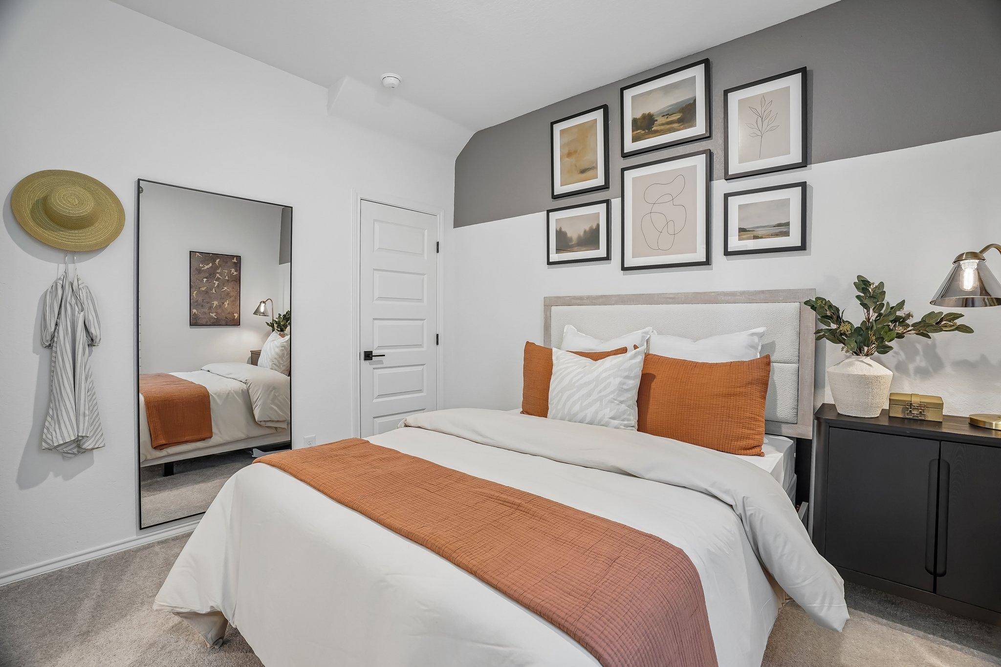 Modern bedroom in Fairway Crossing by Davidson Homes in Converse, TX, featuring a queen bed, gallery wall, and floor mirror.