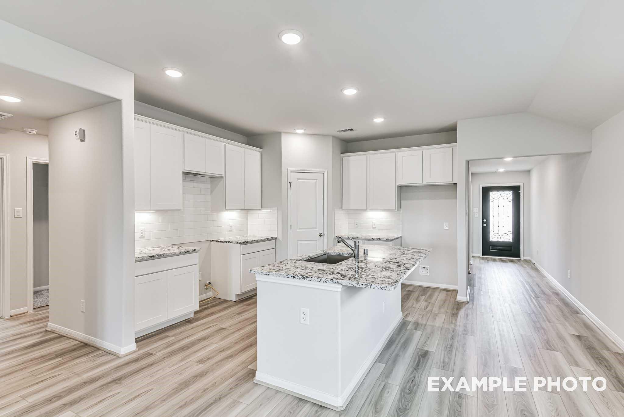 Modern open-concept kitchen featuring white shaker cabinets, quartz island sink, and recessed lighting in Davidson Homes The Riviera A, Rosharon, Texas