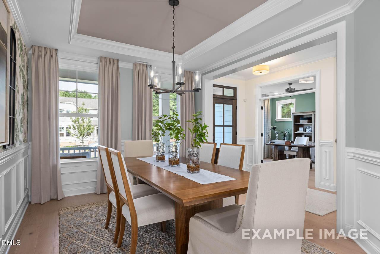 Elegant formal dining room with wooden table, chandelier, and large windows opening to study in Davidson Homes The Crawford D, Angier, NC