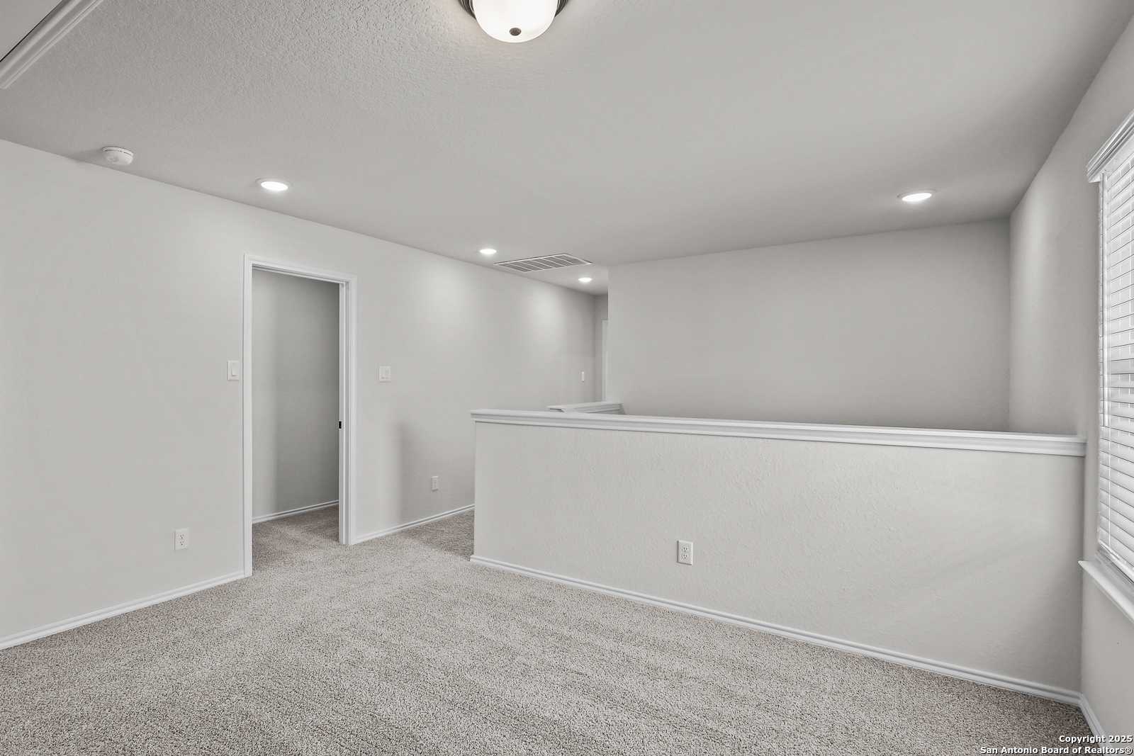 Spacious upstairs landing with white railing, gray carpet, and recessed lighting in Davidson Homes The Florence C, San Antonio