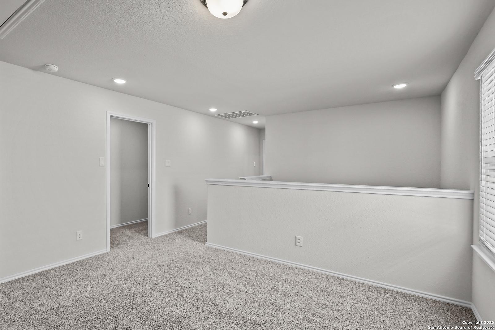Spacious upstairs landing with white railing, gray carpet, and recessed lighting in Davidson Homes The Florence C, San Antonio