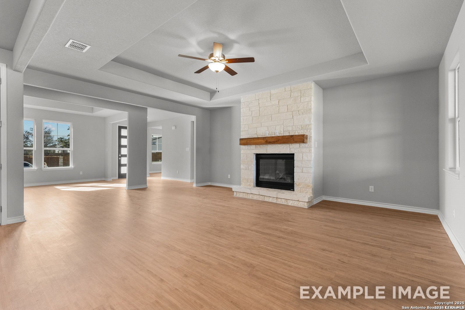 Spacious living room with stone fireplace and tray ceiling in The Oxford F plan at Potranco Oaks, Castroville, Texas.