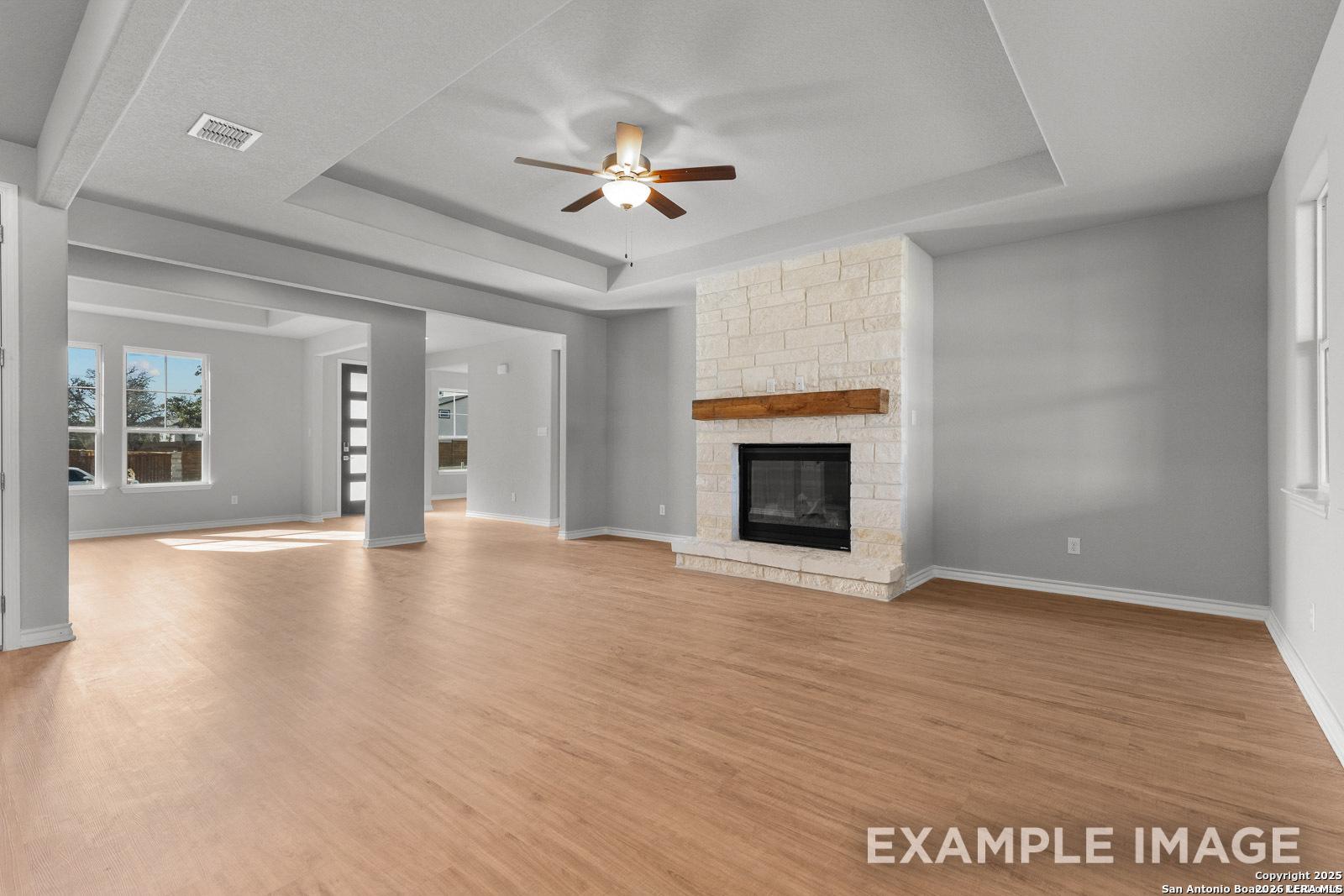 Spacious living room with stone fireplace and tray ceiling in The Oxford F plan at Potranco Oaks, Castroville, Texas.
