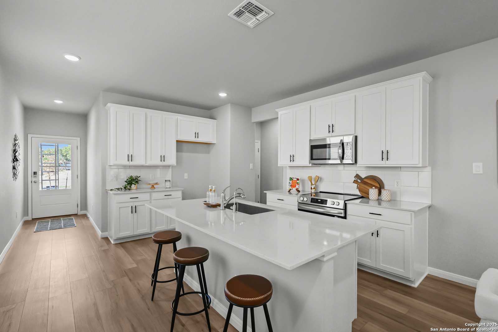 Modern white kitchen with quartz island, stainless appliances, and bar stools in Davidson Homes The Gillian C, San Antonio, Texas