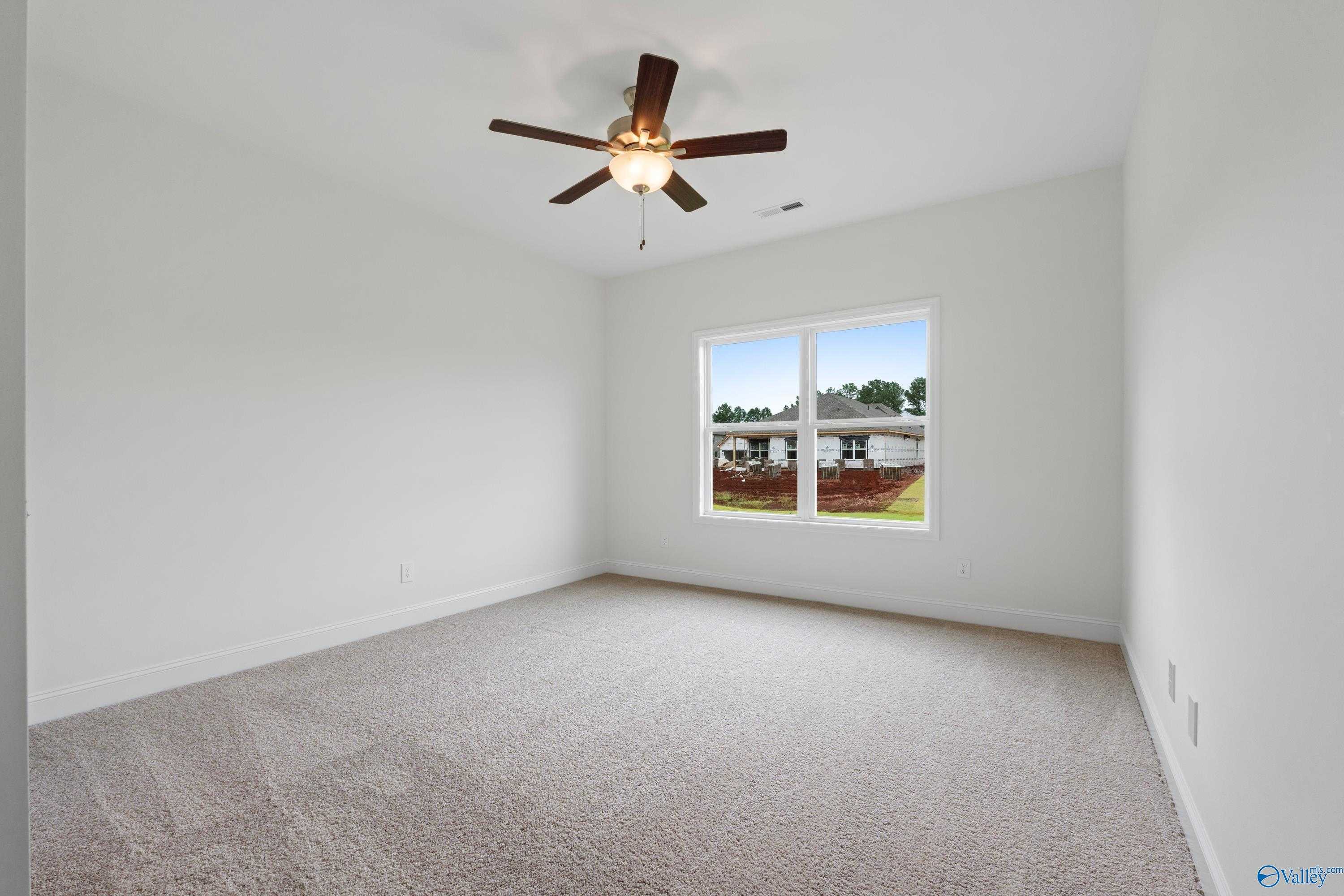 Spacious empty bedroom with ceiling fan, beige carpet, and large window overlooking yard in Davidson Homes Asheville C, Athens AL