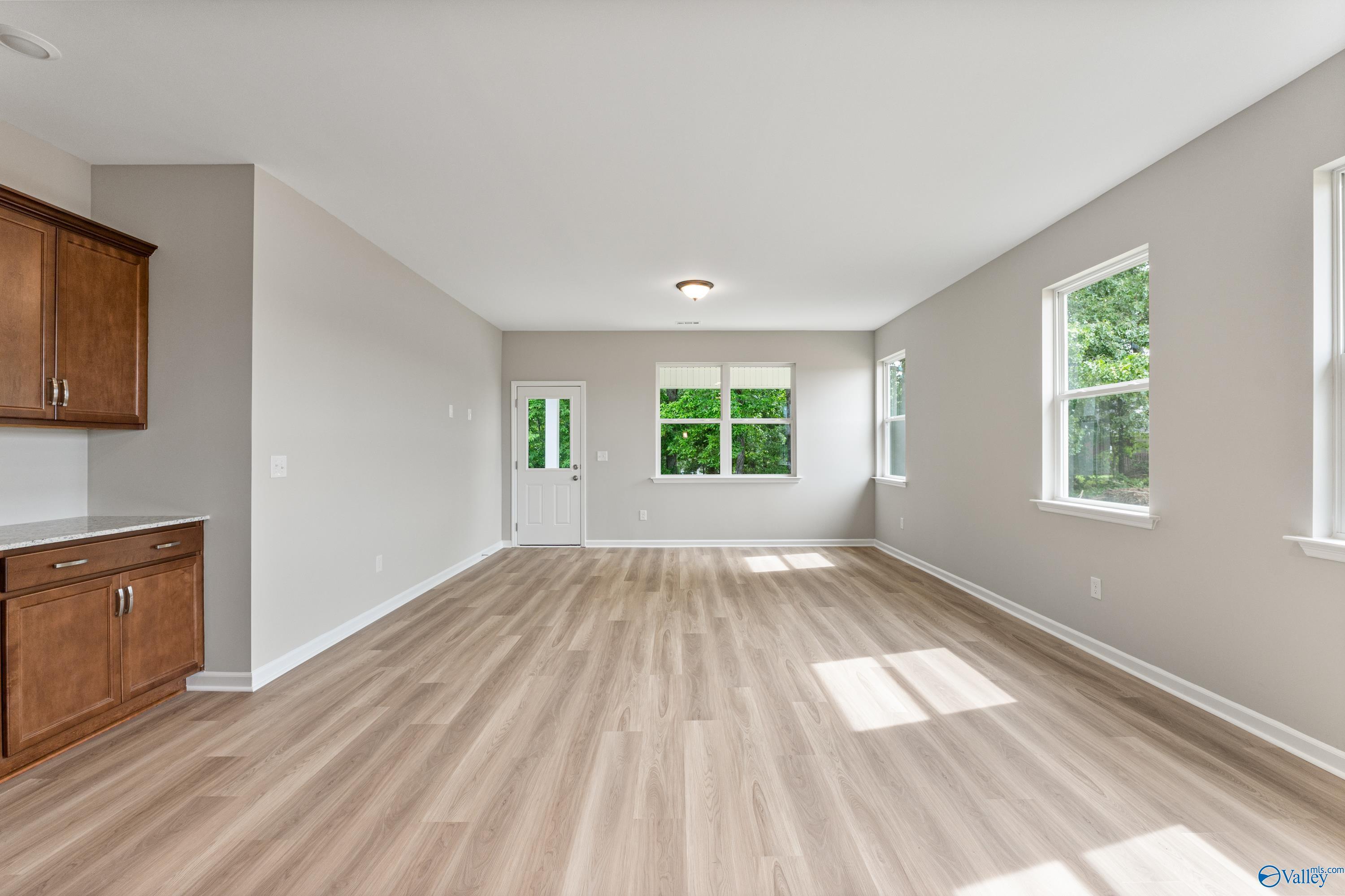 Spacious open living area with light hardwood floors, large windows, and adjacent kitchen cabinets in The Aurora 4-bedroom home, Fayetteville, TN