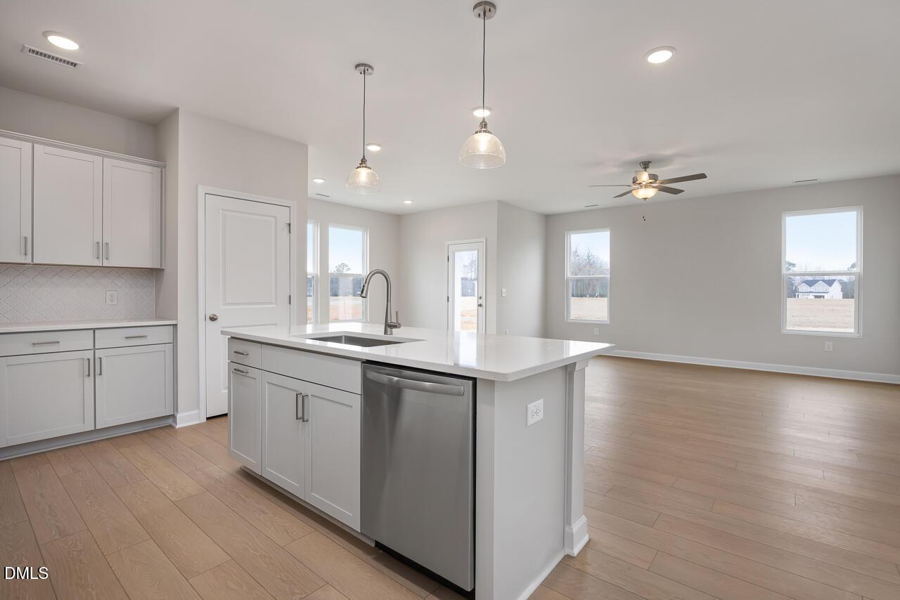 Modern open-concept kitchen with white shaker cabinets, island farmhouse sink, stainless dishwasher, pendant lights in The Daphne C, Lillington NC