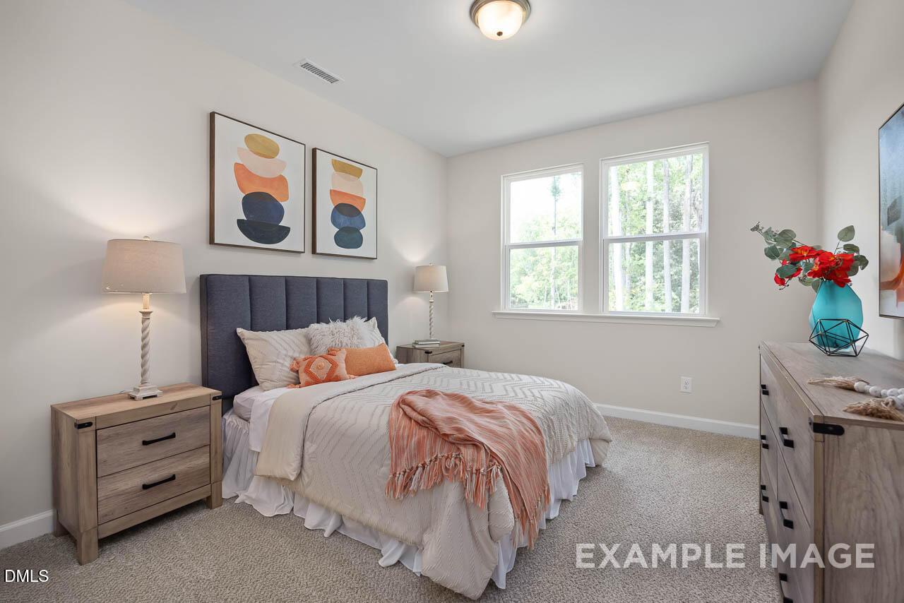 Cozy secondary bedroom with gray tufted headboard, plush bedding, abstract art, and tree views in Davidson Homes The Willow D, Lillington