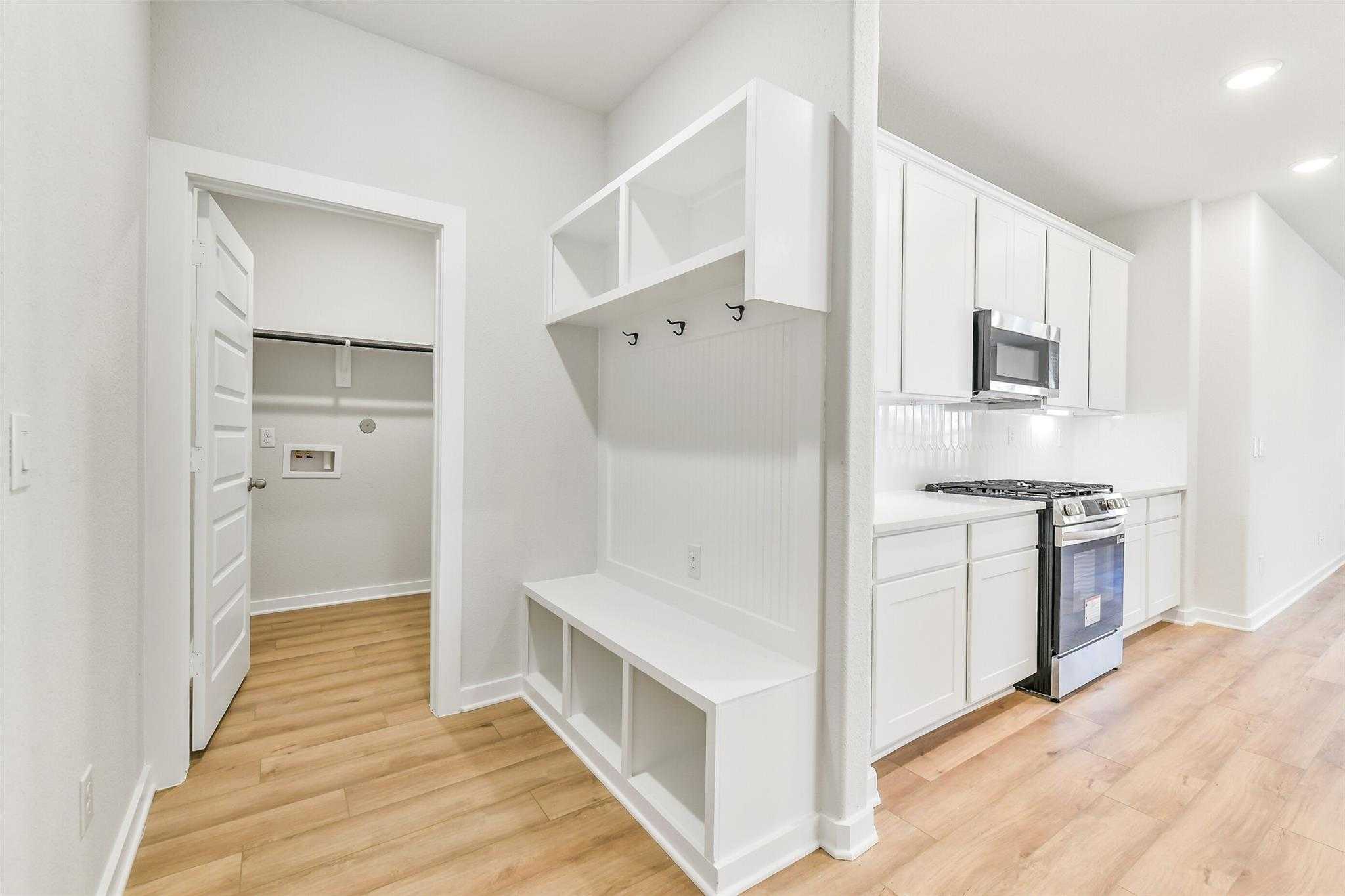 White mudroom with built-in bench, coat hooks, open shelves, and laundry access in Davidson Homes The Blanco E, Magnolia Texas