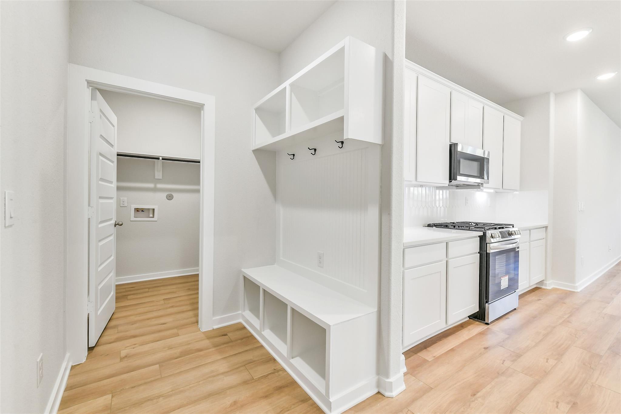 White mudroom with built-in bench, coat hooks, open shelves, and laundry access in Davidson Homes The Blanco E, Magnolia Texas