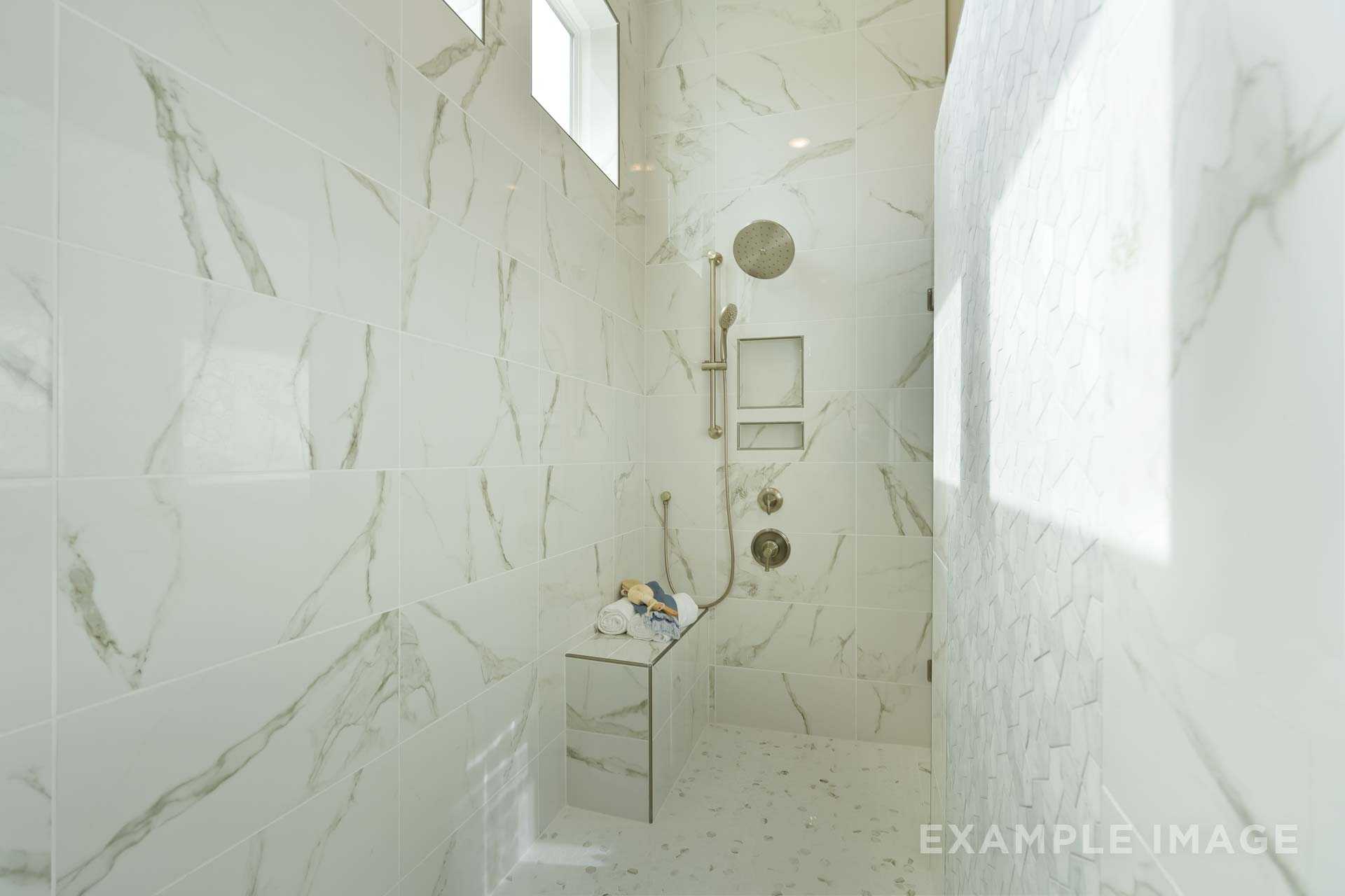 Luxury walk-in shower in The Seaside master bath with white marble tiles, rainfall head, bench, and glass enclosure