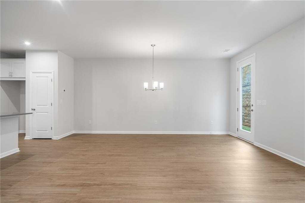 Spacious open living-dining area with hardwood floors, white kitchen cabinets, and chandelier in Davidson Homes The Cary A, Kennesaw, Georgia