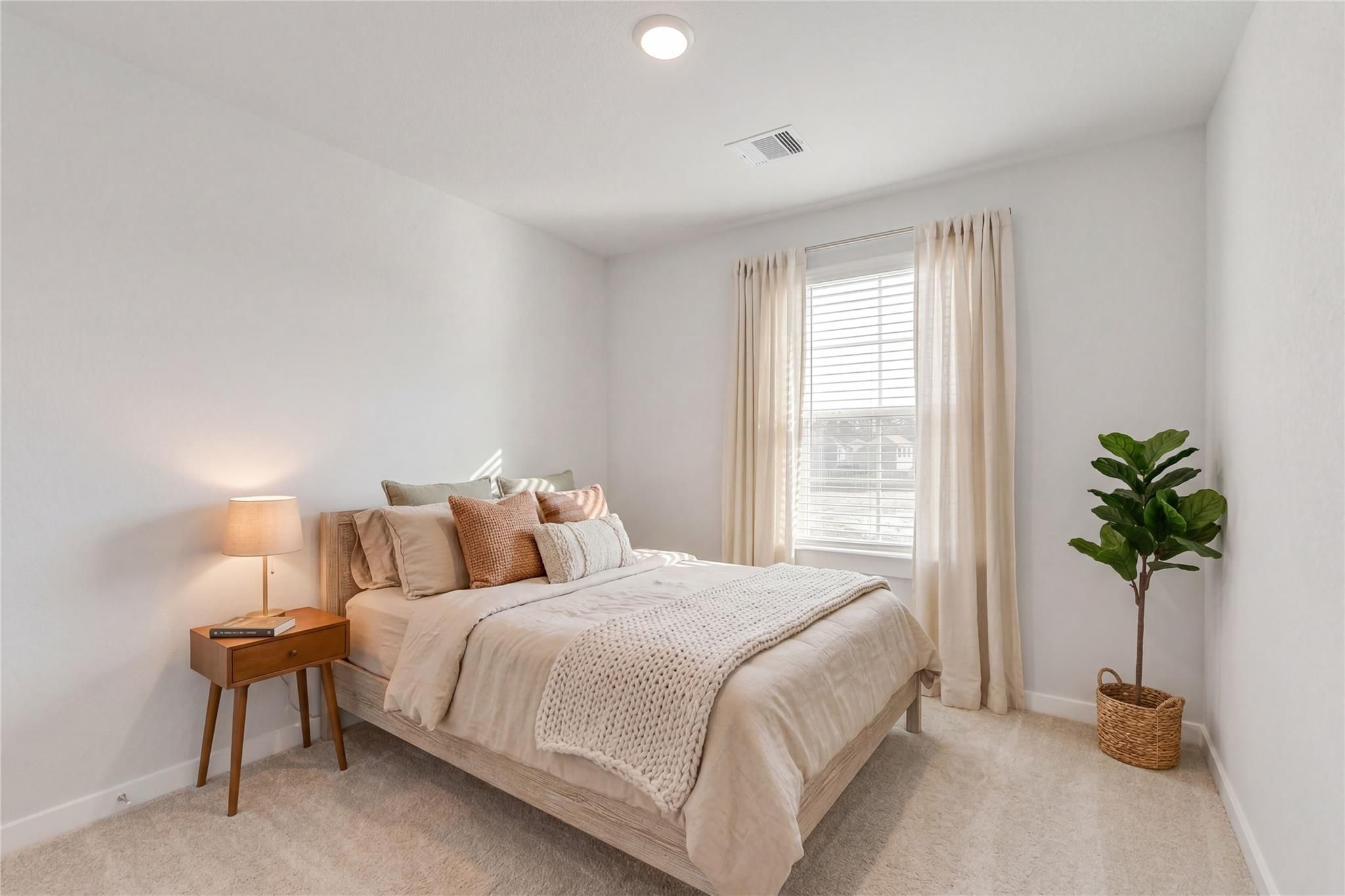 Cozy bedroom with beige bedding, sheer-curtained window, nightstand lamp, potted plant in Davidson Homes The Brazos E, Cleveland, Texas