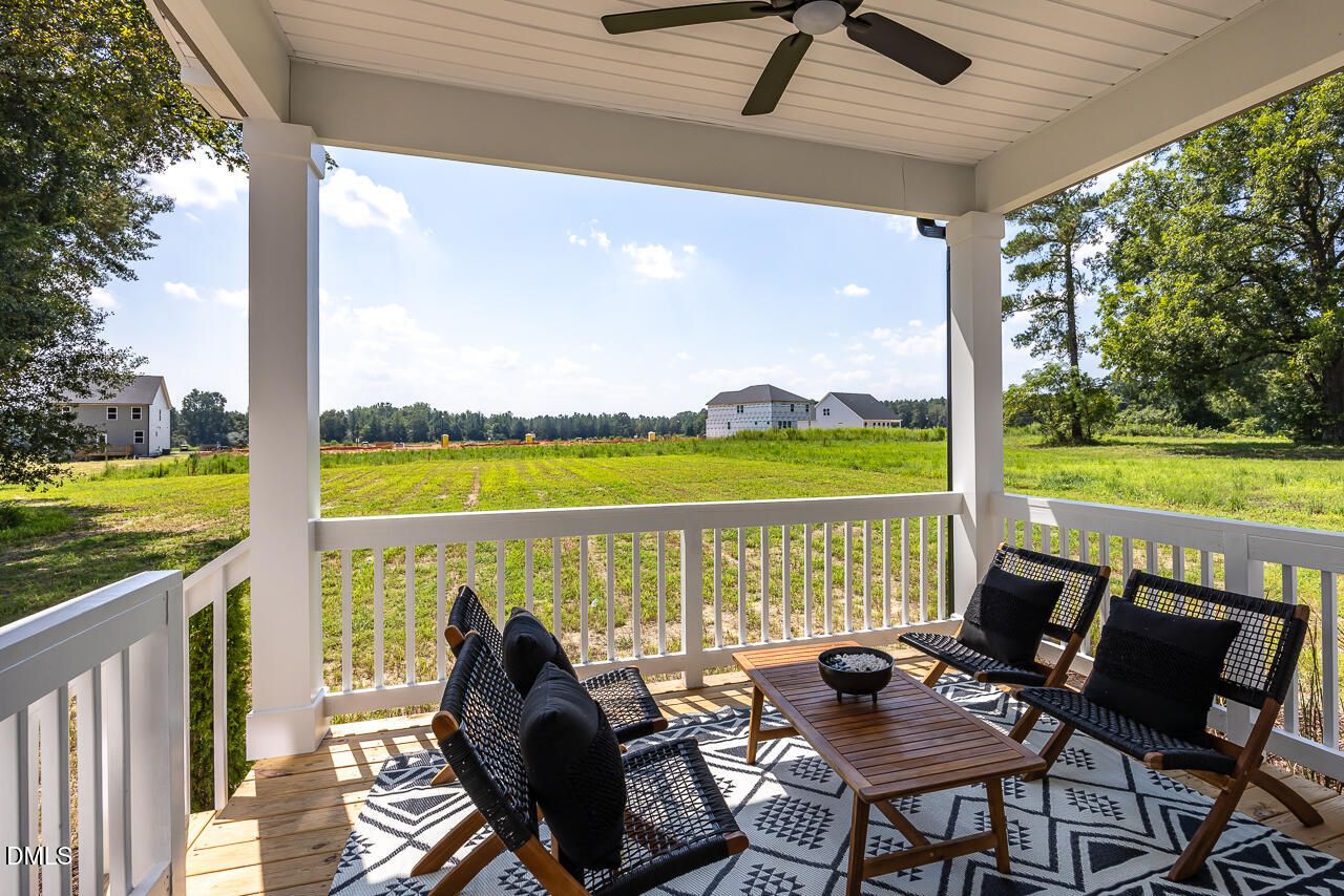 Covered back patio with wicker seating, ceiling fan, overlooking green fields and woods in Woodland Crossing, Zebulon, NC