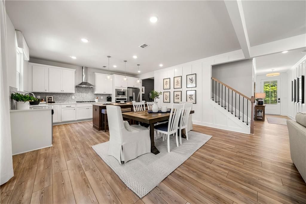 Open-concept kitchen with white cabinets, island, and stainless appliances adjacent to dining area with wooden table in Davidson Homes The Willow B, Riverwood, Dallas, Georgia