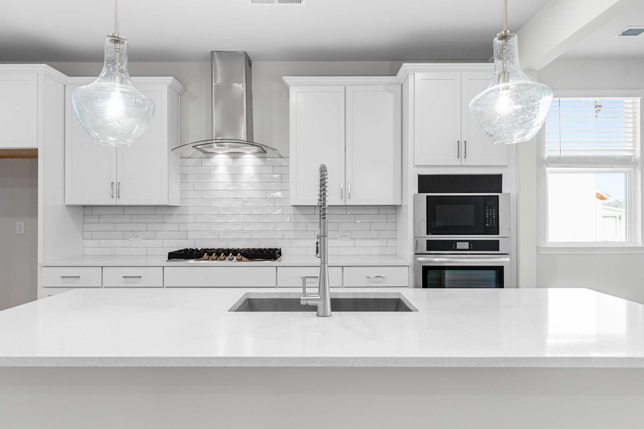 Modern white kitchen in The Glenwood A with quartz island sink, subway tile backsplash, glass pendants, stainless appliances