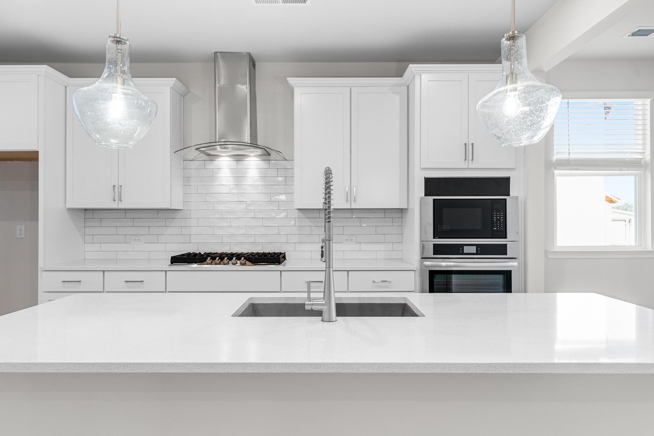 Modern white kitchen in The Glenwood A with quartz island sink, subway tile backsplash, glass pendants, stainless appliances