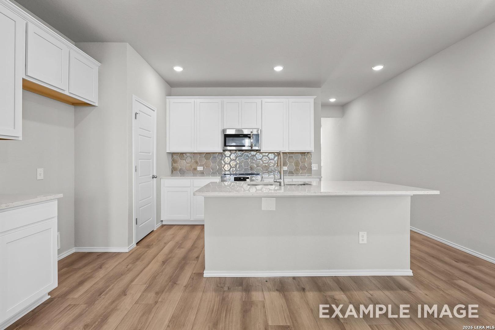 Modern kitchen with quartz island, white cabinets, and tile backsplash in The Colorado B at Applewhite Meadows, San Antonio.