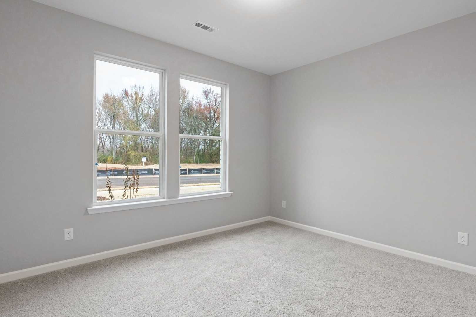 Spacious empty bedroom in The Luna home with gray walls, large double windows overlooking trees, and neutral carpet flooring