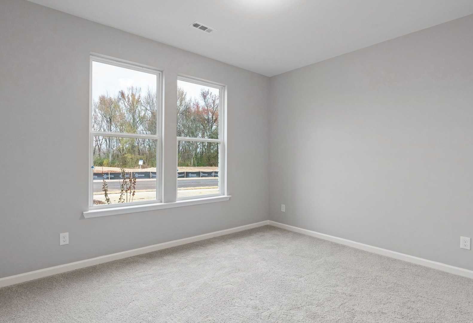 Spacious empty bedroom in The Luna A with light gray walls, carpeted floor, and large windows overlooking trees