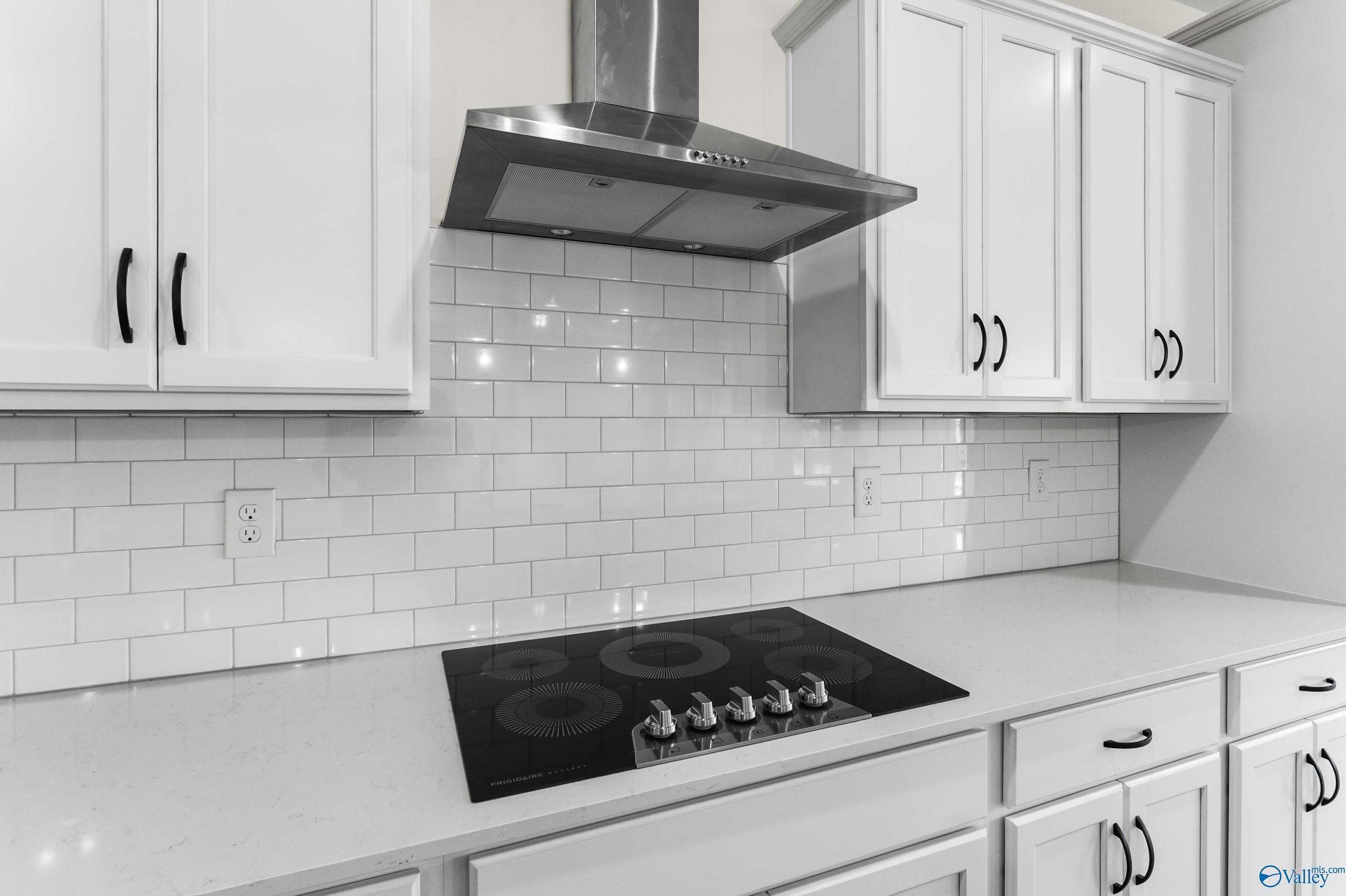 Modern kitchen featuring white shaker cabinets, subway tile backsplash, stainless range hood, and gas cooktop in The Finleigh by Davidson Homes, Harvest, AL