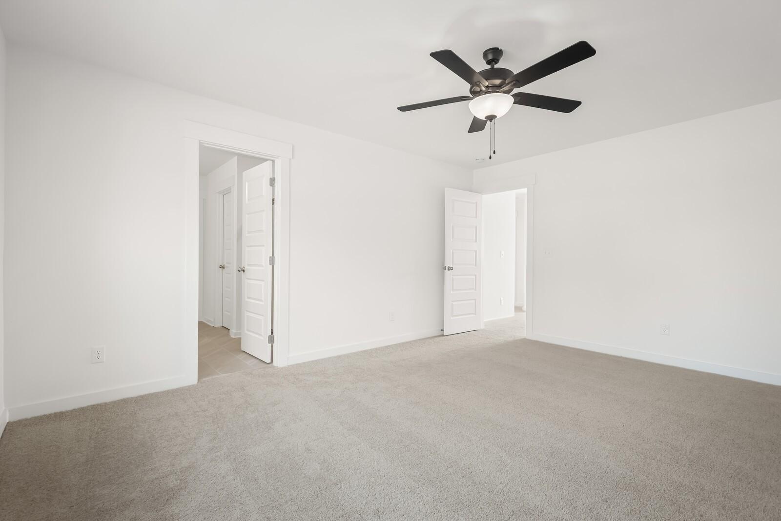 Bright bedroom with ceiling fan, beige carpet, and open doors to adjacent rooms in Davidson Homes The Logan C, Gallatin, TN