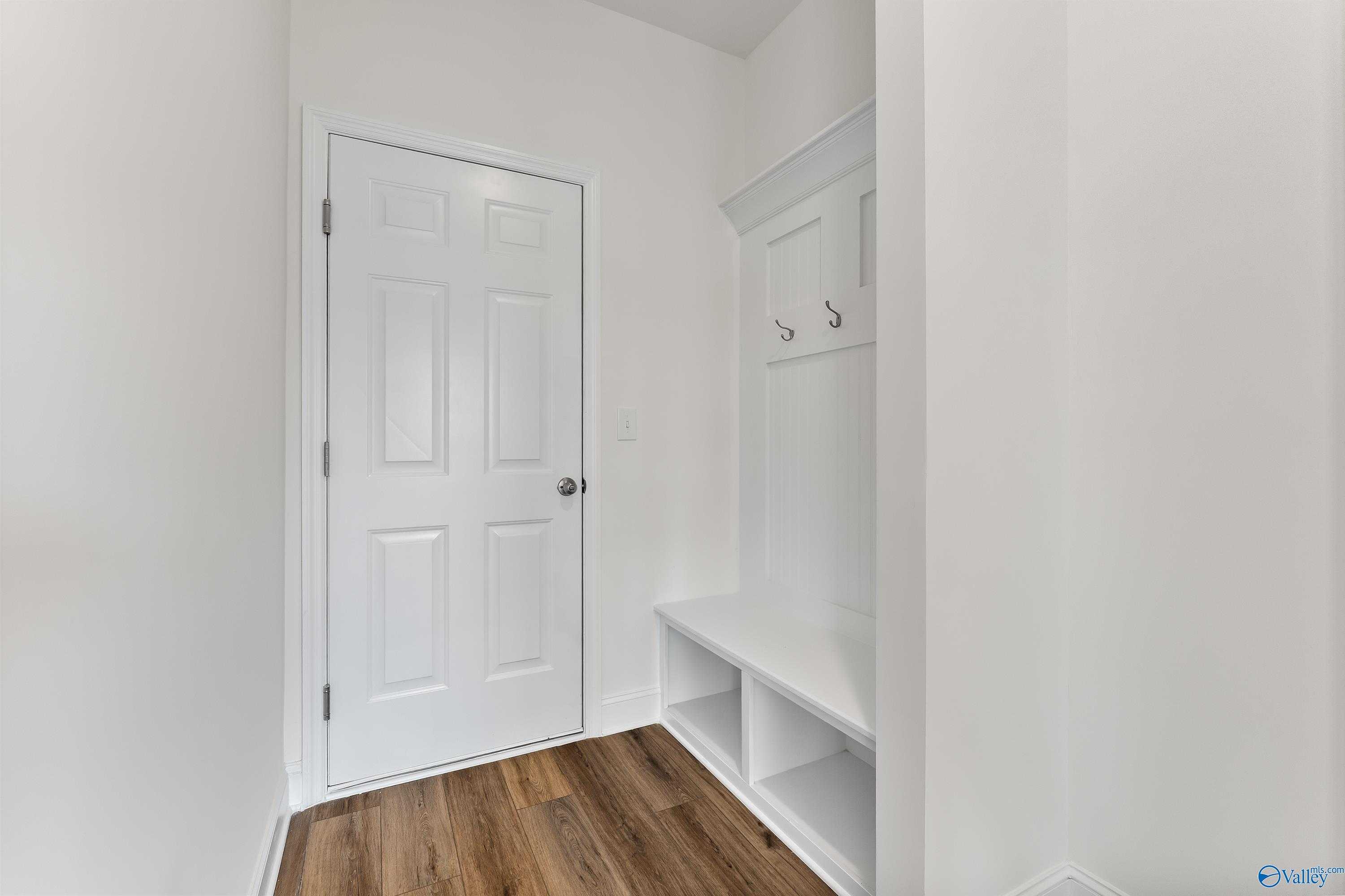 Bright mudroom with white built-in coat hooks, bench, shelves, and paneled door in Davidson Homes The Shelby A, New Market, AL