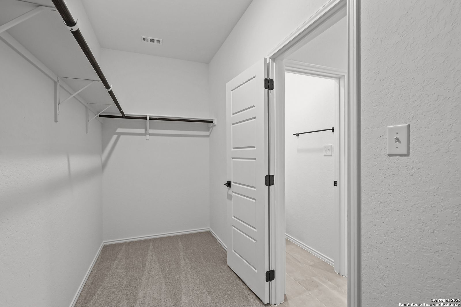 Spacious walk-in closet with white walls, hanging rods, shelves, and open door in master suite, Davidson Homes The Daphne J, Converse Texas