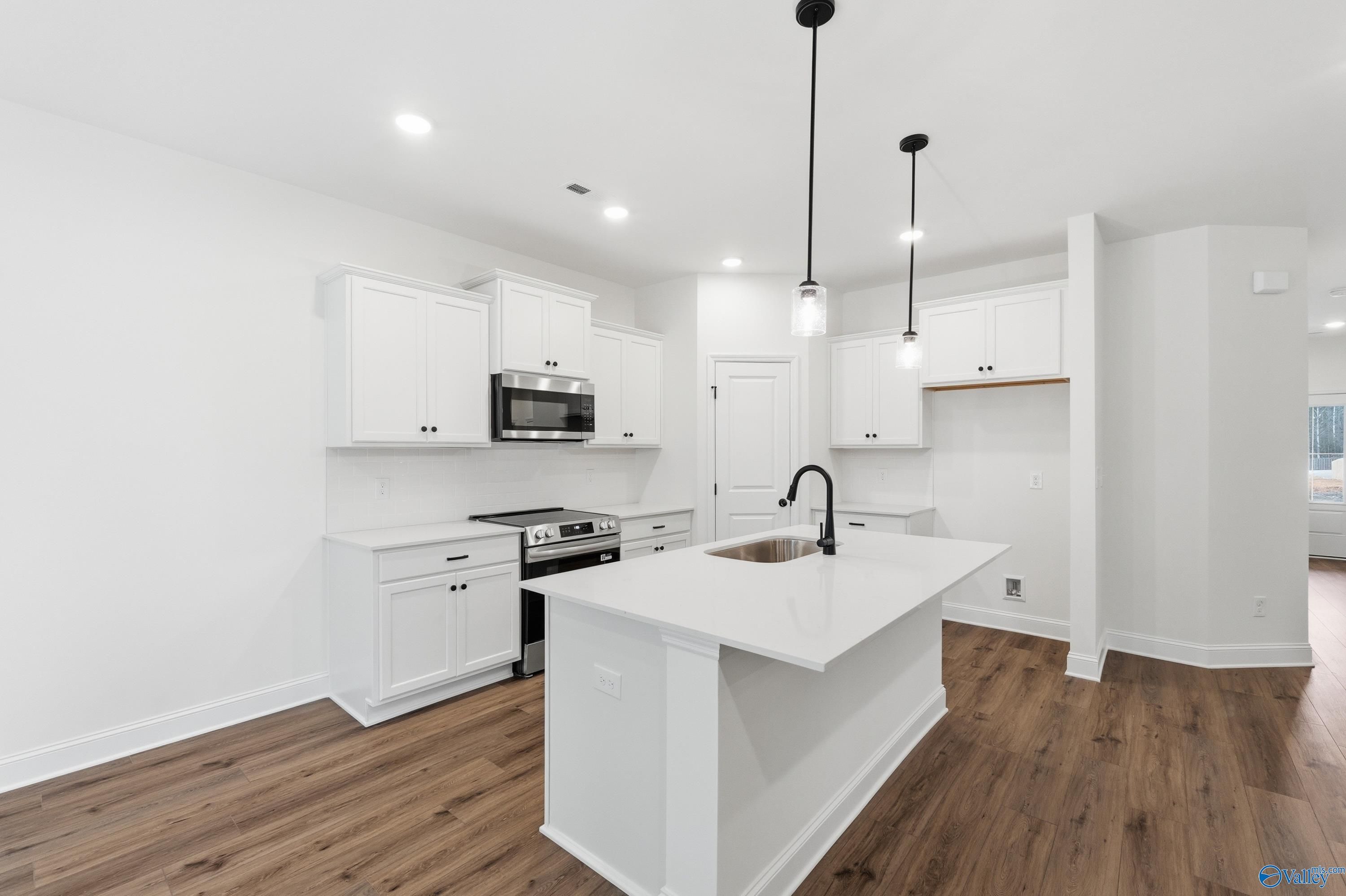 Modern white kitchen with island, stainless appliances, pendant lights in Davidson Homes The Asheville C, Arab, AL