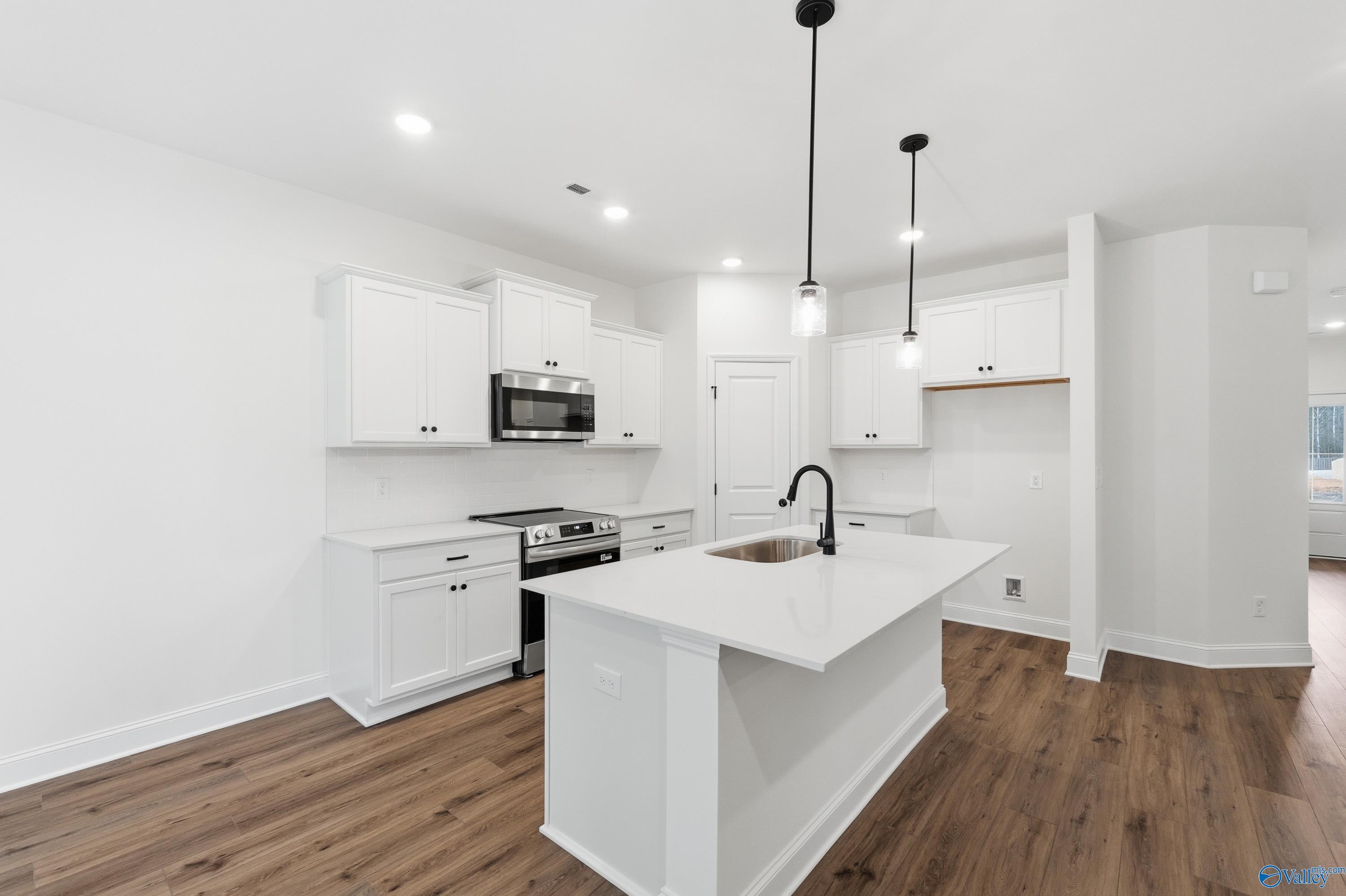 Modern kitchen with white cabinetry, center island, and stainless appliances in The Asheville C plan at The Highlands, Arab.