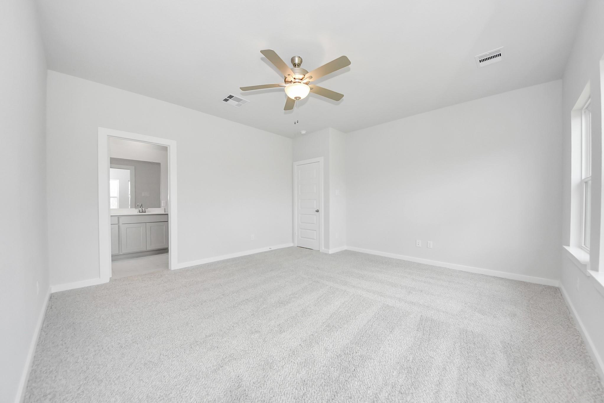 Bright primary bedroom with carpet and ceiling fan in The Verano B floor plan by Davidson Homes in Sunterra, Katy, Texas.