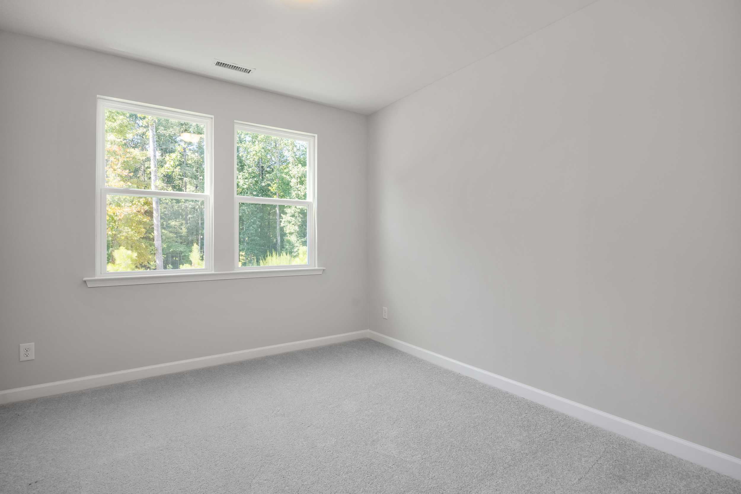 Spacious upstairs bedroom in The Aspen C featuring large windows with wooded views, light gray walls, and carpet flooring