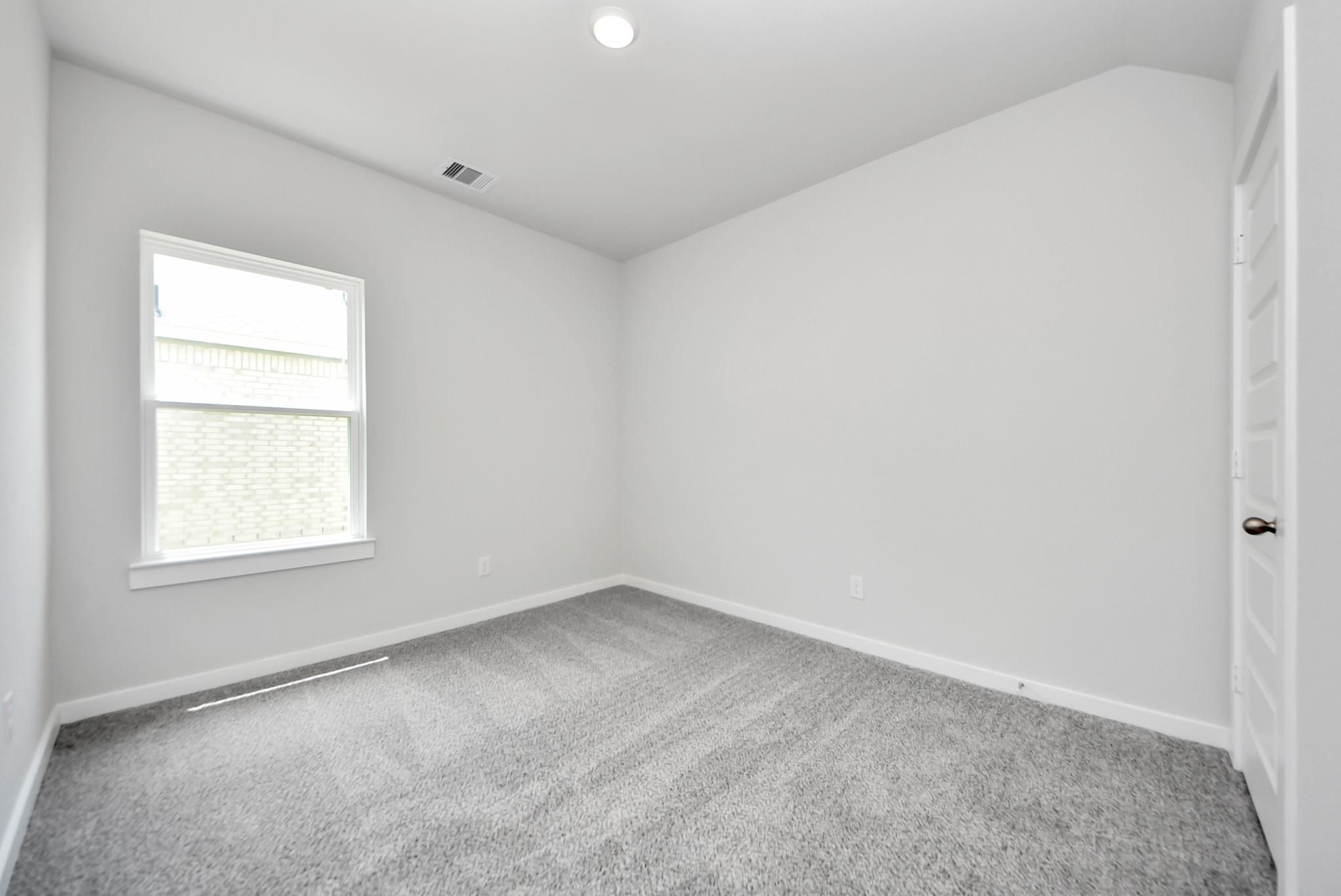 Bright, spacious secondary bedroom with neutral gray carpet in The Sabine E floor plan at Windmill Estates, Magnolia, TX.