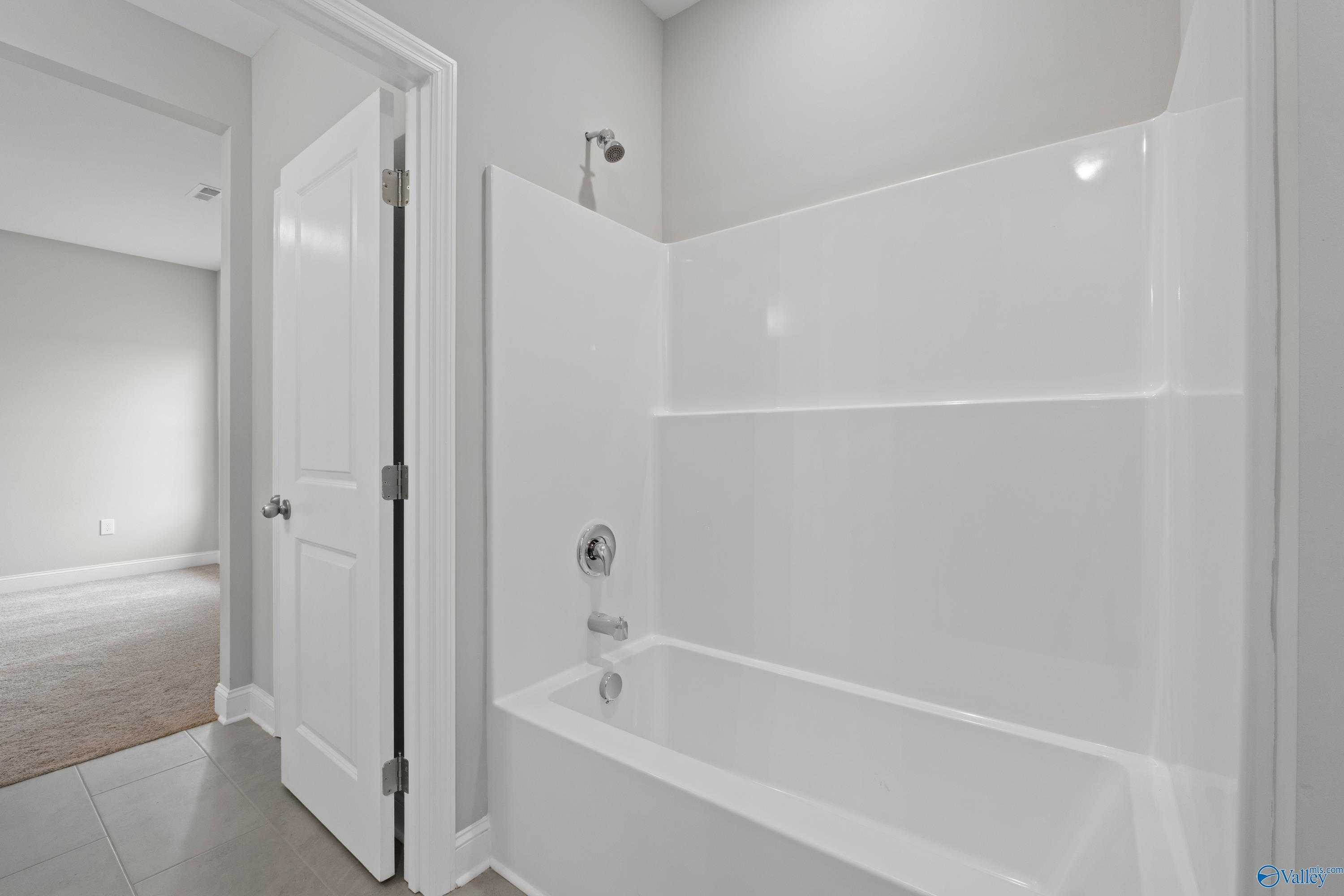 Bright master bathroom with white tub, glass shower enclosure, and neutral tones in Davidson Homes The Finleigh, Briercreek, Alabama