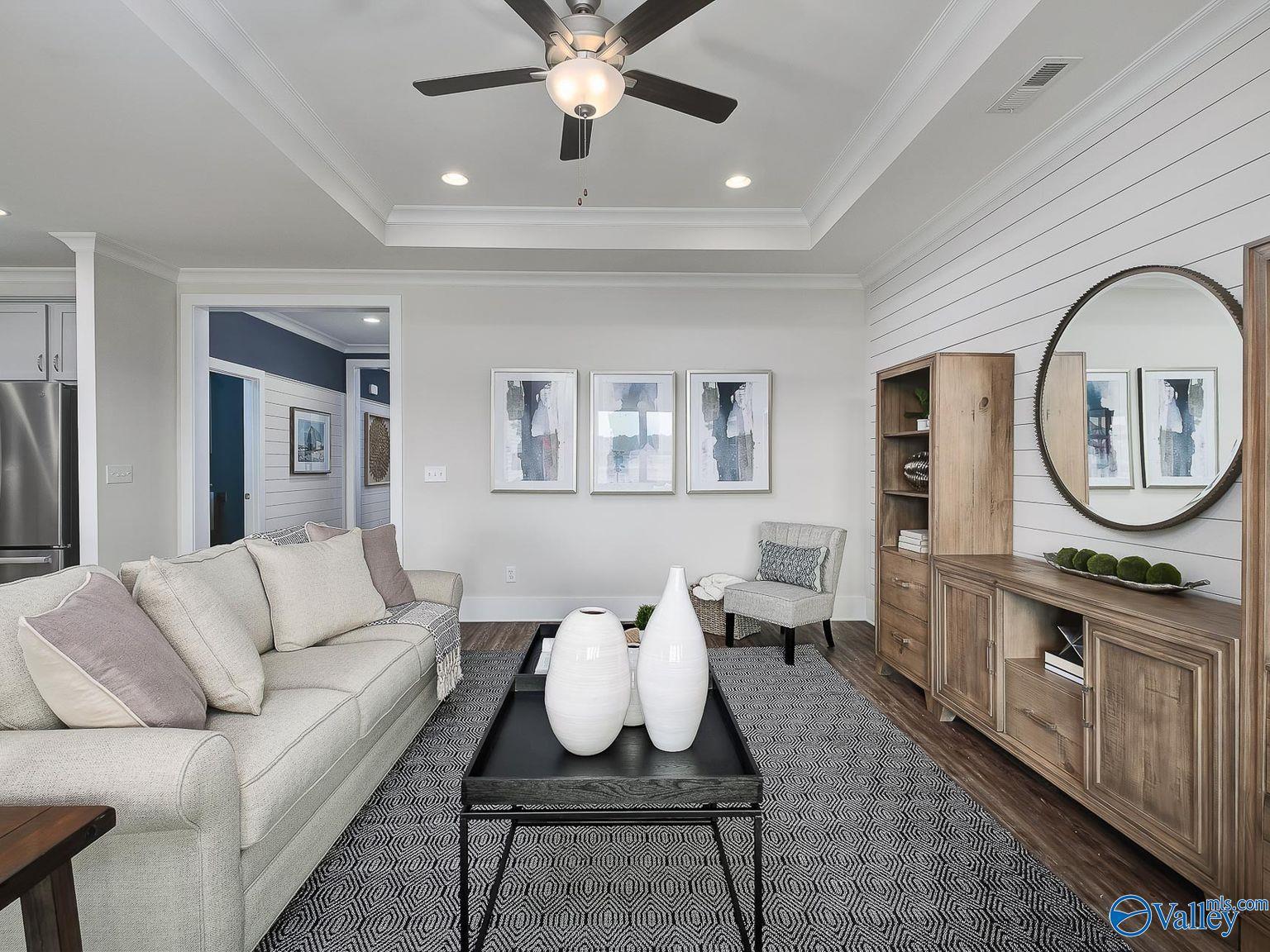 Cozy living room with neutral sofa, ceiling fan, abstract art, and open kitchen in Davidson Homes The Everett, Toney, Alabama