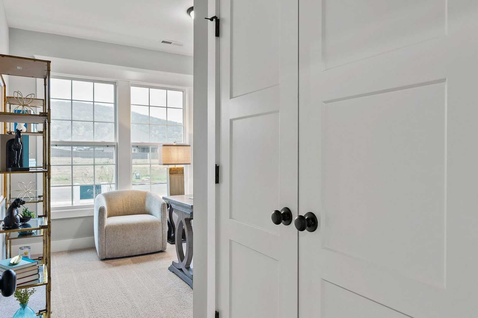 Cozy study in The Oxford home design with built-in bookshelves, mountain view window, armchair, and open white doors