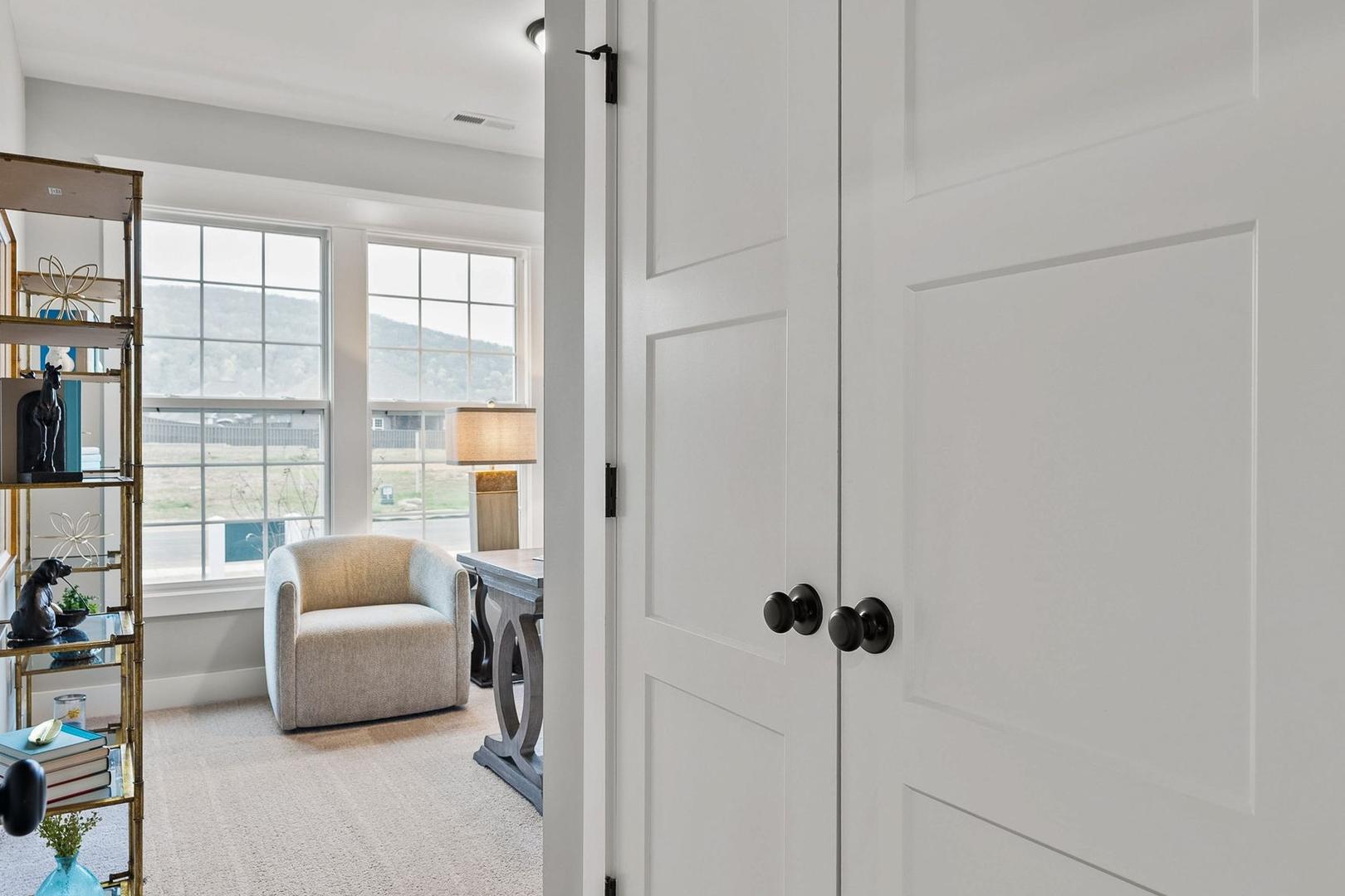 Cozy study in The Oxford home design with built-in bookshelves, mountain view window, armchair, and open white doors