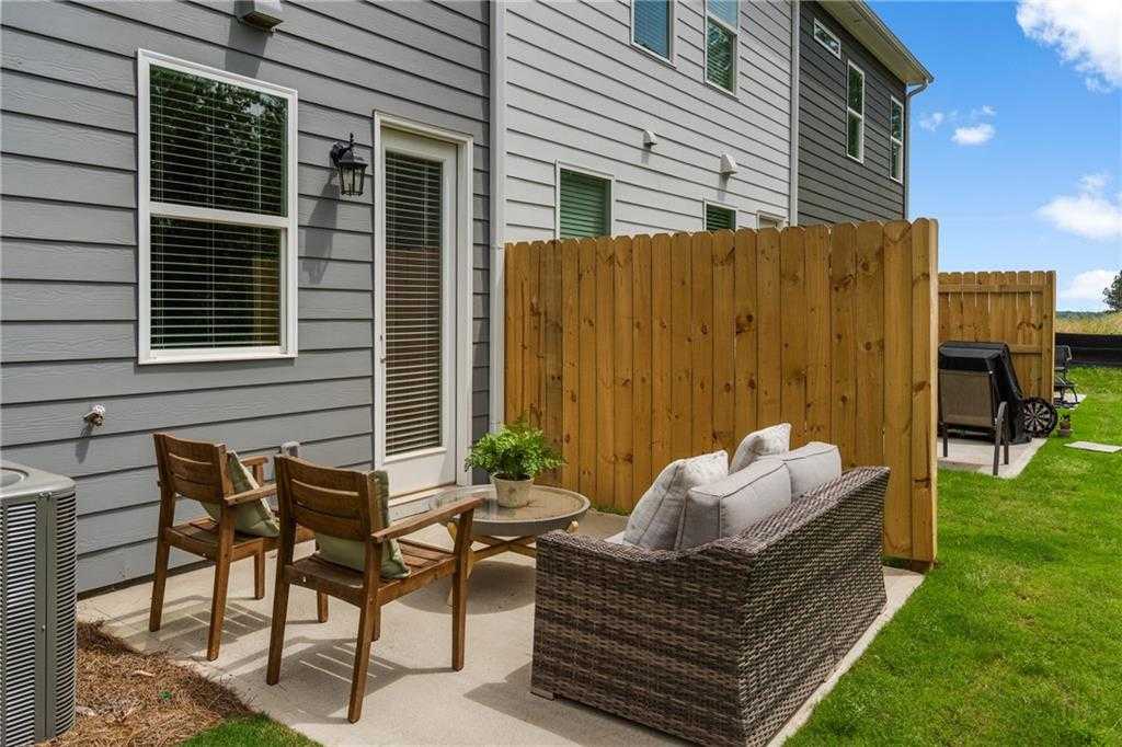 Covered back patio with wicker sofa, cushioned wooden chairs, round table, potted plant, wooden fence, lush green yard in The Durant A, Stegall Village, Emerson, GA