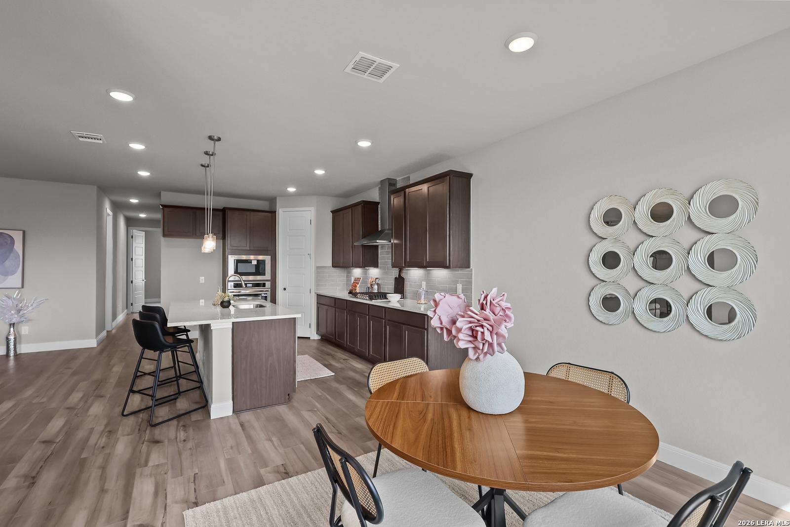 Modern open-concept kitchen with dark wood cabinets, white island, pendant lights, and adjacent dining table in Davidson Homes The Rockford G, Ladera, San Antonio