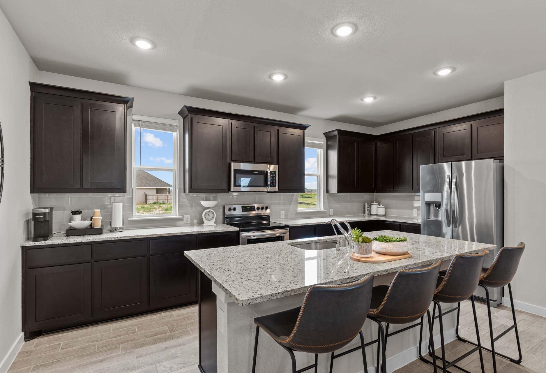 Spacious modern kitchen in The Collin A home featuring dark cabinets, quartz island, stainless appliances, and bar stools